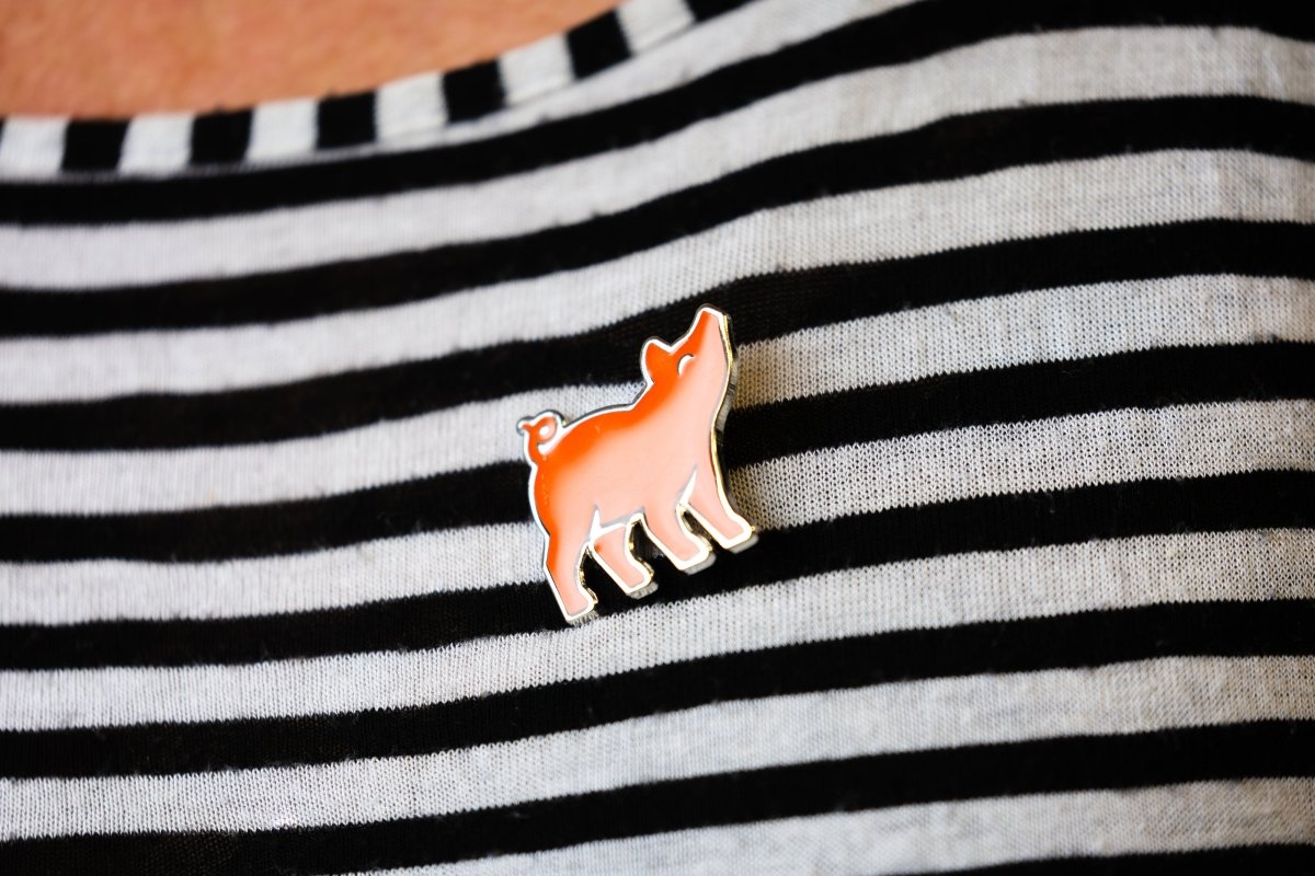 An orange metal pin badge pinned to a black and white striped top.