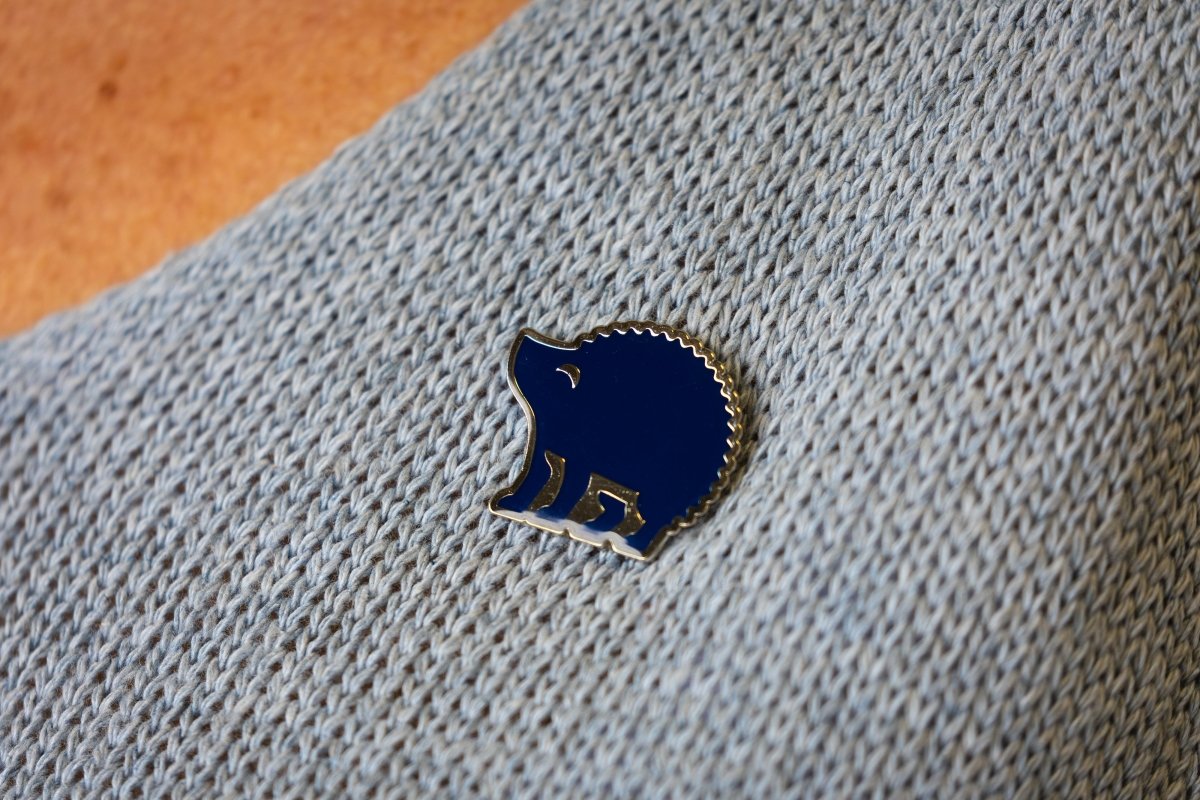 A dark blue hedgehog metal pin badge pinned to a grey knitted jumper.