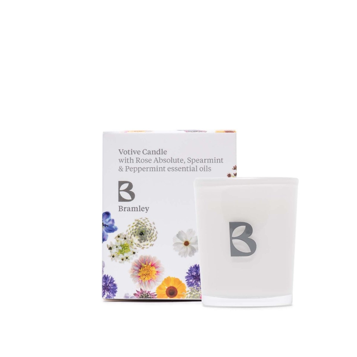 A glass votive candle, placed next to a white gift box decorated with flowers.