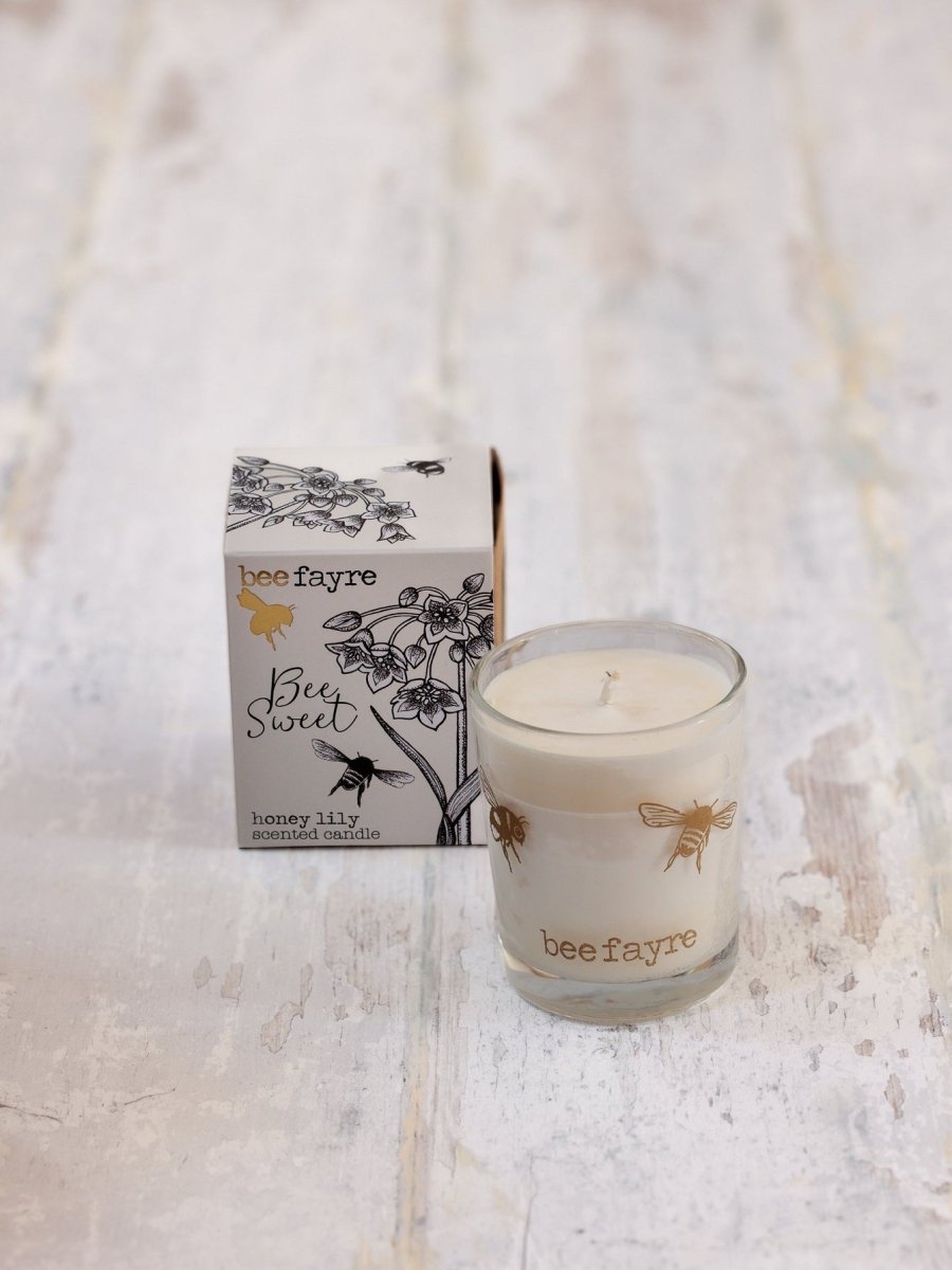 A glass honey lily scented candle placed next to a gift box.