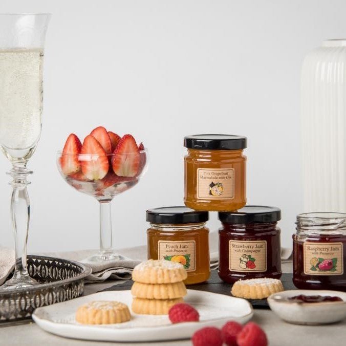 An afternoon tea, with four jam pots, champagne, strawberries and biscuits.