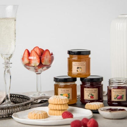 An afternoon tea, with four jam pots, champagne, strawberries and biscuits.