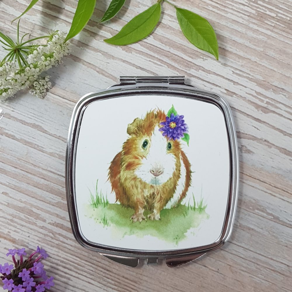 The closed lid design of the Pollyanna Compact Mirror. It features a watercolour painting of a white and ginger Guinea Pig with a flower in its hair.