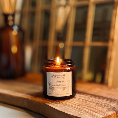 A lit soy wax candle with a white label on the front, the candle is sat on a wooden board, lit in a house.