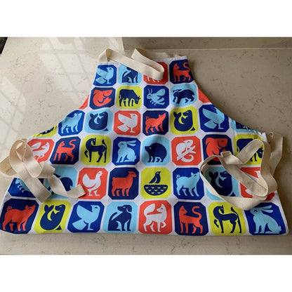 An apron printed with different animal graphics on it, folded up and laid on a kitchen floor. 