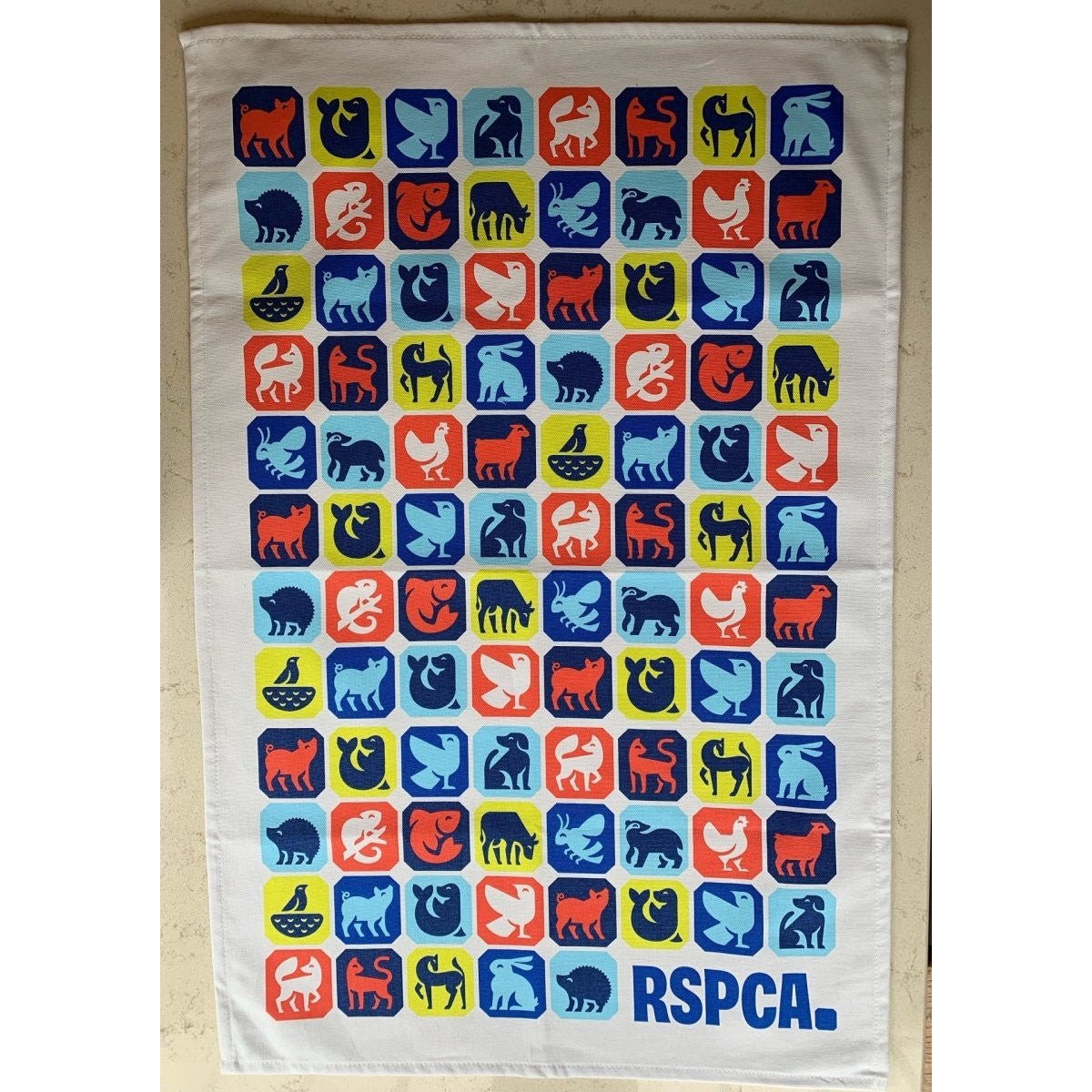 An RSPCA tea towel printed with different animal graphics and a blue RSPCA logo.