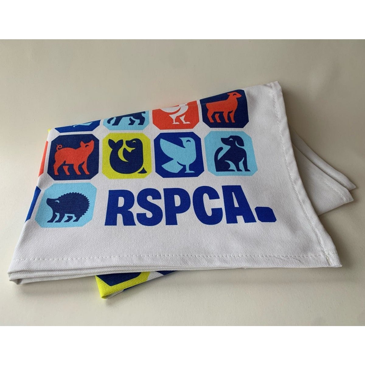 A folded RSPCA tea towel printed with different animal graphics and a blue RSPCA logo.